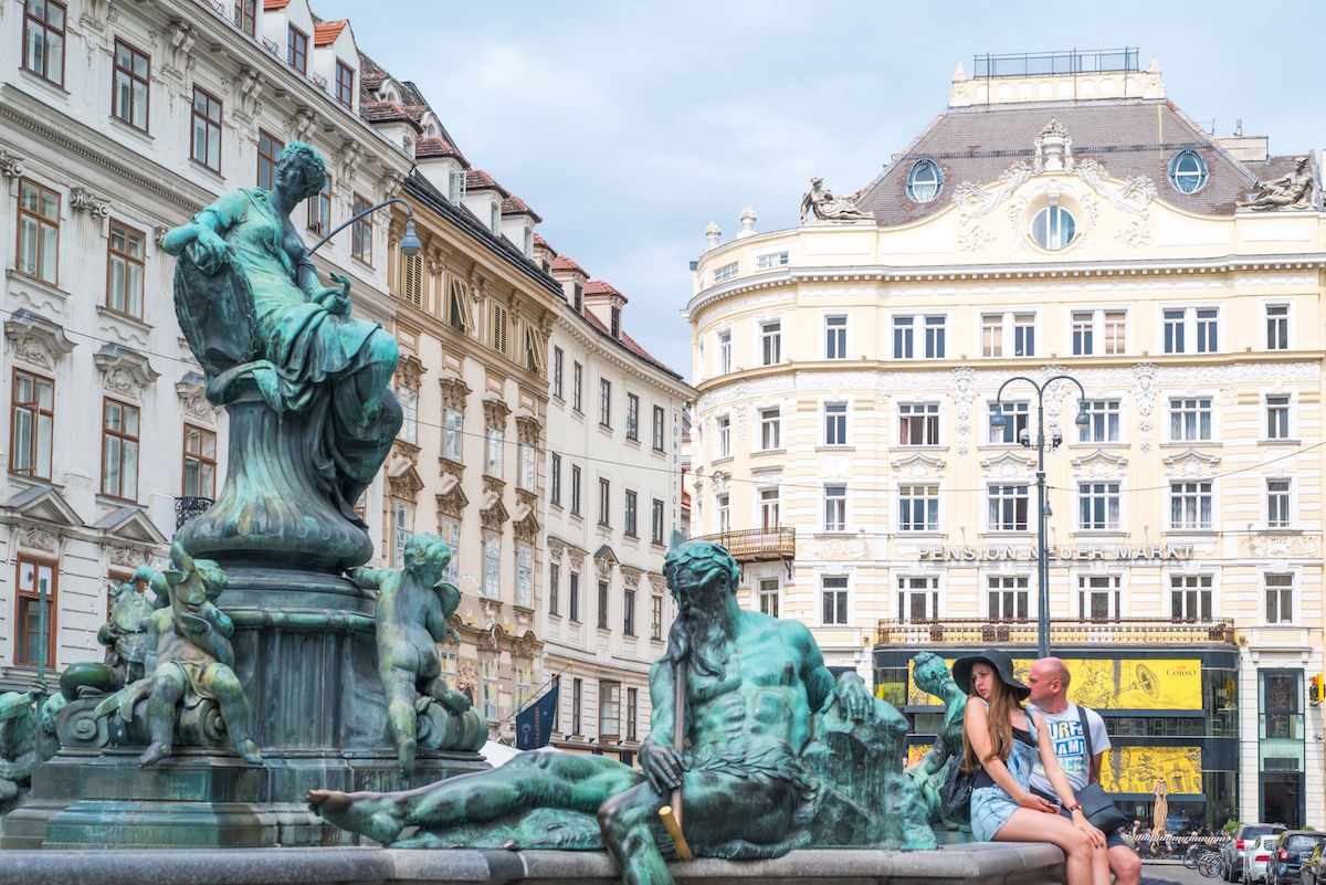 Austria, Vienna, Tourists sitting on the fountain of Market square